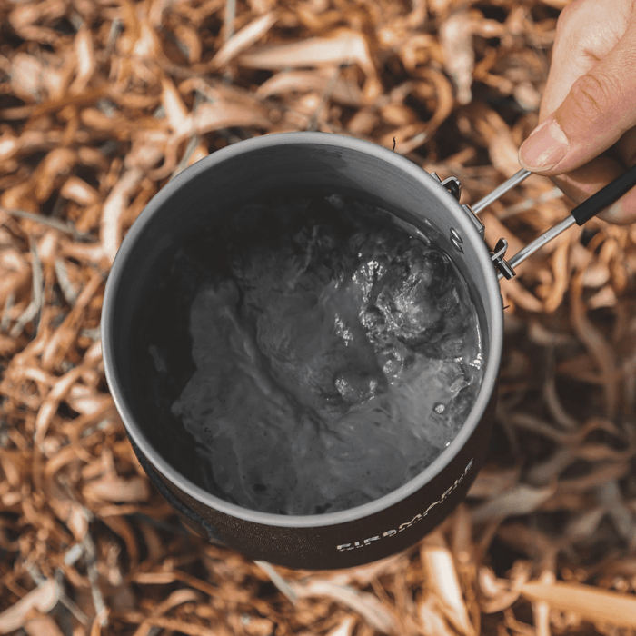 Person holding a camping mug with ice cubes against a natural background#color_black-red