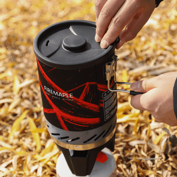 FireMaple camping stove being adjusted outdoors on a leafy background #color_black-red