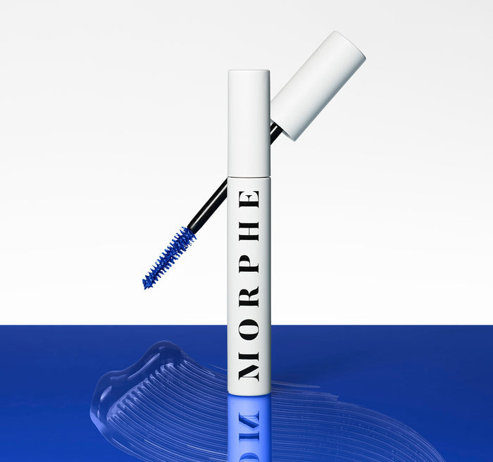 Morphe The Big Prime Lash Primer white tube labeled MORPHE with blue-bristled wand and blue primer swatch on glossy blue surface.
