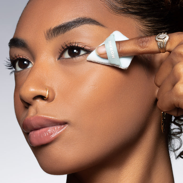 Model applying the Morphe To The Point Dual Sided Powder Puff Green to her cheekbone, with "MORPHE" text visible on the light blue puff edge.
